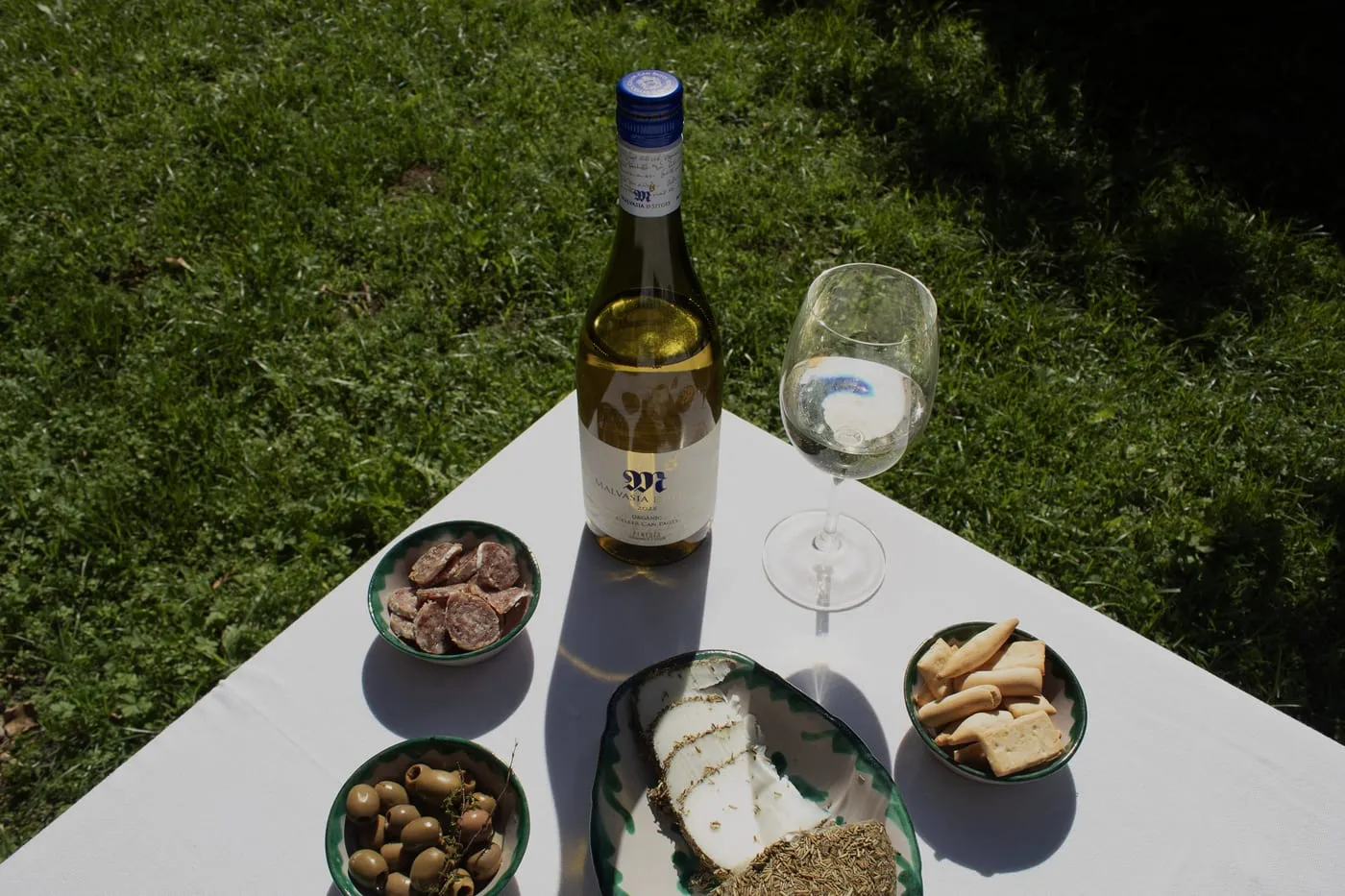 Mesa con una botella de Malvasia de Sitges y maridaje de embutidos, queso y olivas